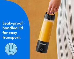 A closeup of a woman's hand, carrying the portable blender near her hip. She is wearing loose, striped white pants. A blue panel to the left of the image reads: "Leak-proof handled lid for easy transport". A circular icon beneath the text shows an illustration of a hand gripping the handled lid of the blender.