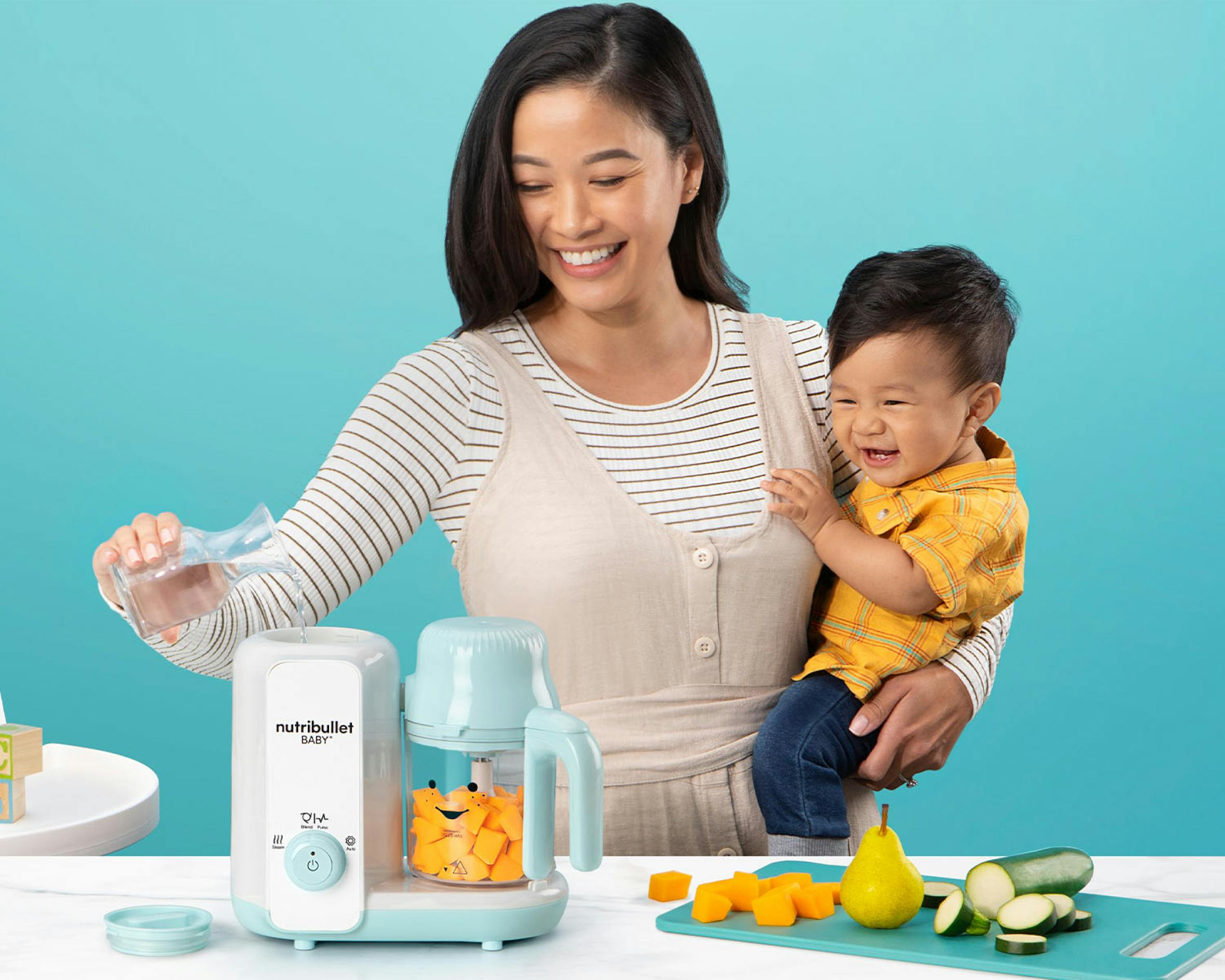 Mom and baby adding veggies and water to the baby steam and blend