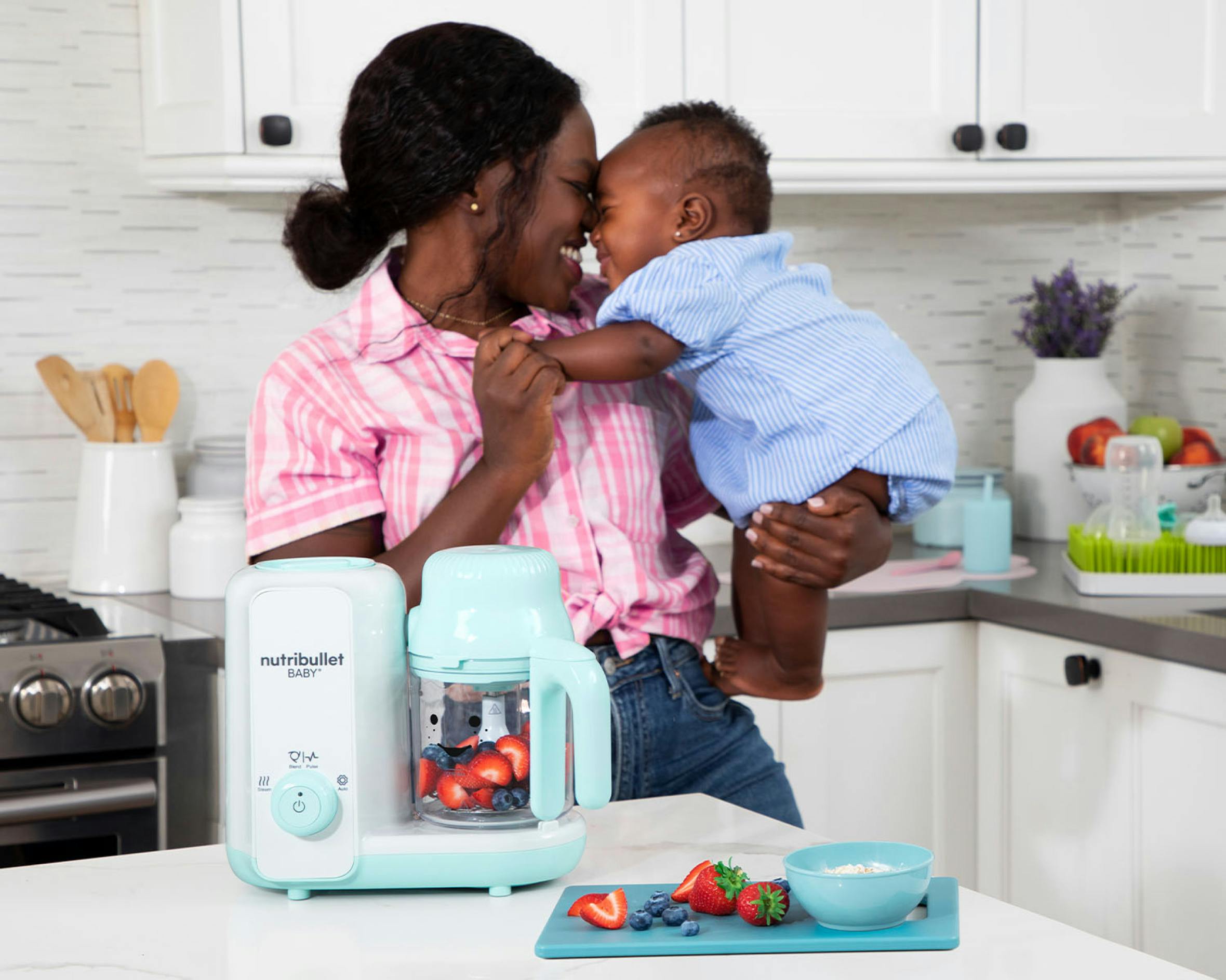Mom and baby with the baby steam and blend filled with berries in the kitchen