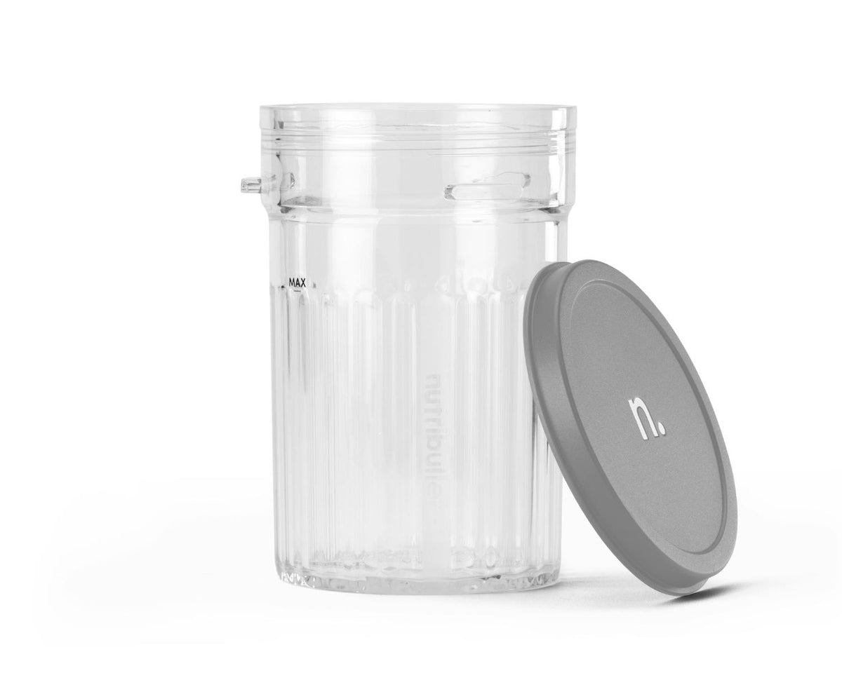 A clear plastic ribbed cup with a max fill line next to a grey circular lid propped against the side.