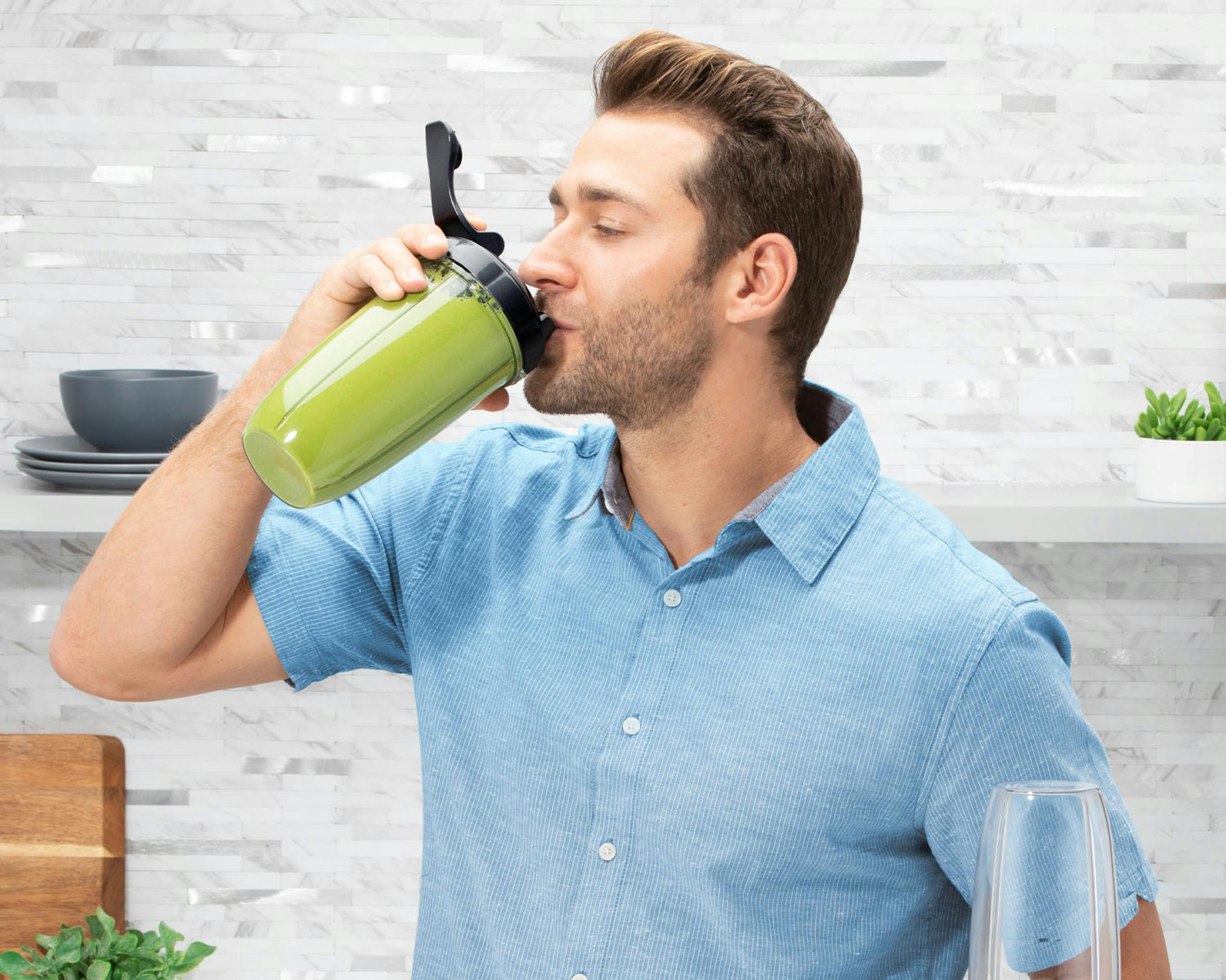 man drinking a green smoothie in the kitchen