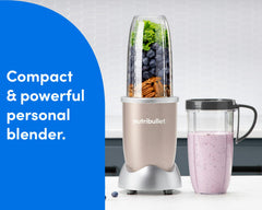 The nutribullet Pro rests on a white countertop. The Tall Cup is attached to the Power Base and filled with a variety of unblended fruits and vegetables. A Tall Cup with the Handled Lip Ring attached rests to the right of the blender, filled with a light pink smoothie.