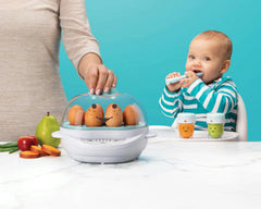 NutriBullet Baby Steamer with eggs next to fruits and veggies with mother's hand and baby eating in background.